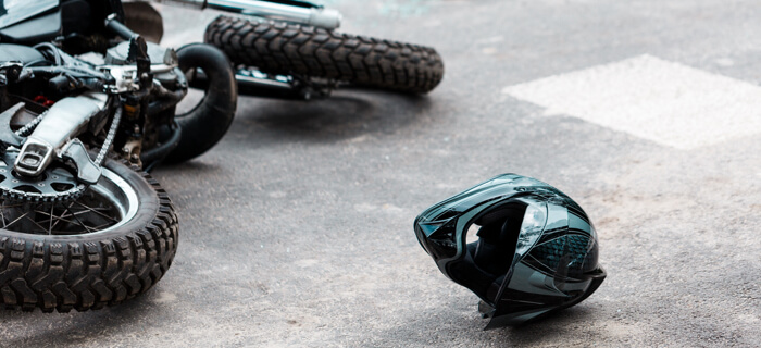 una moto volteado cerca de un carro chocado, con su ventana rota. un casco queda solo en la pista